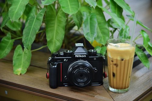 Free A Nikon Zf camera next to an iced coffee amidst lush green leaves, outdoors. Stock Photo