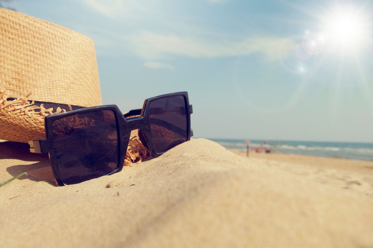 close up of sunglasses and straw hat on sandy beach under bright sunli