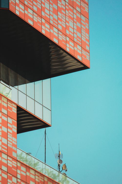 Free A striking modern building with red geometric patterns contrasts against a clear blue sky. Stock Photo