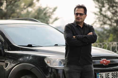 Free A man wearing glasses and a black shirt stands confidently beside a black SUV outdoors. Stock Photo
