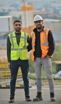 Two construction workers wearing safety vests and hard hats at a construction site.