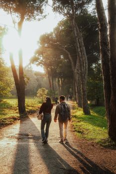 A couple walks hand-in-hand along a sunlit forest path, creating a serene autumn scene.