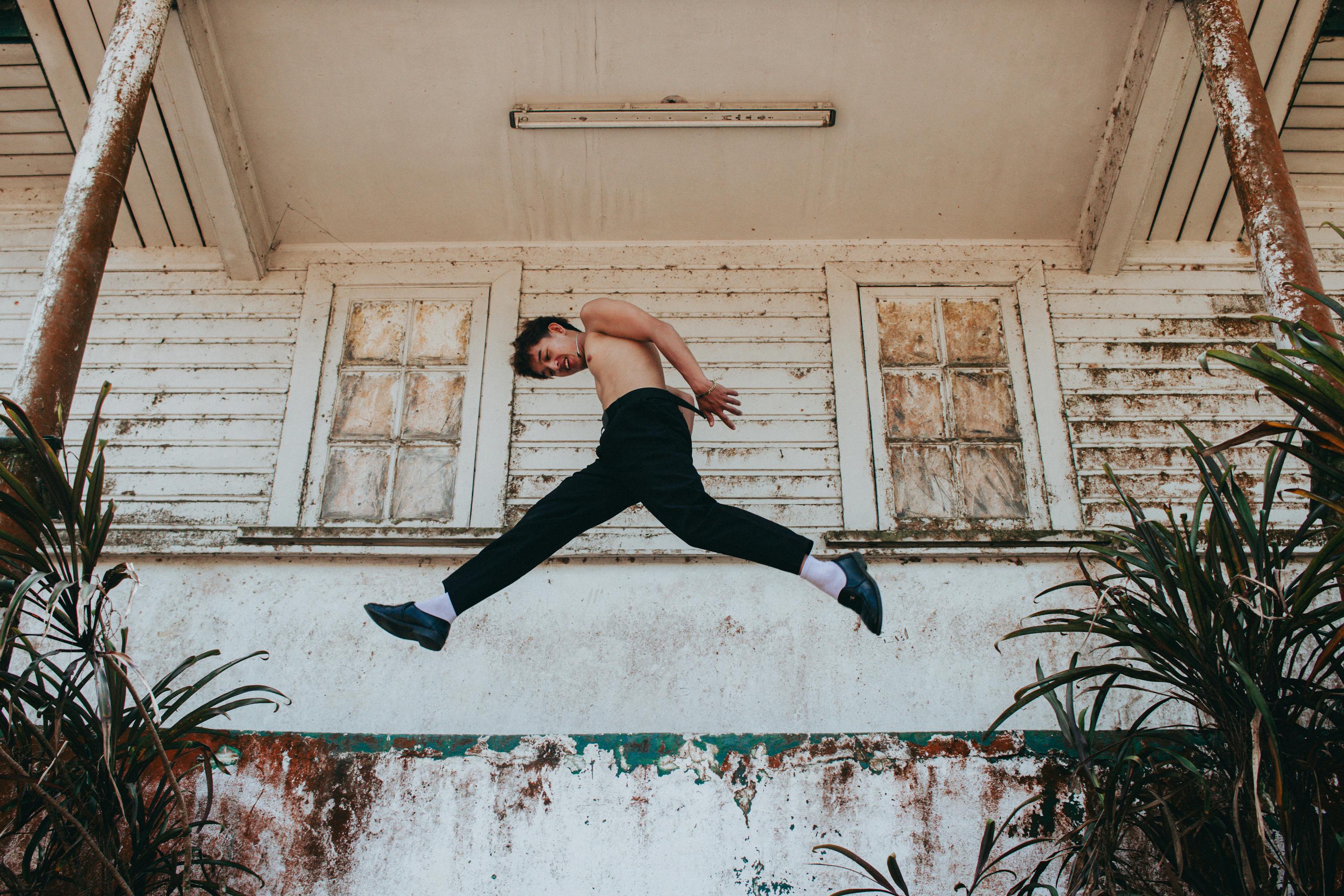 Man gracefully jumps mid-air in front of an aged wooden building, exuding motion and freedom.