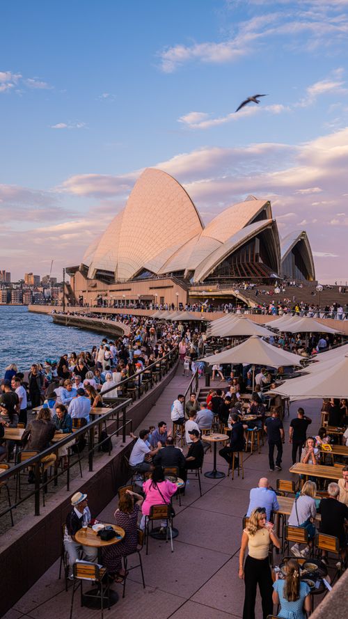 Free Tourists and locals enjoy a vibrant evening at Sydney Opera House, New South Wales, Australia. Stock Photo