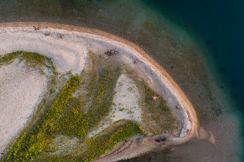 Free Aerial photo capturing the unique curvature of a sandy shoreline with lush vegetation by the water. Stock Photo