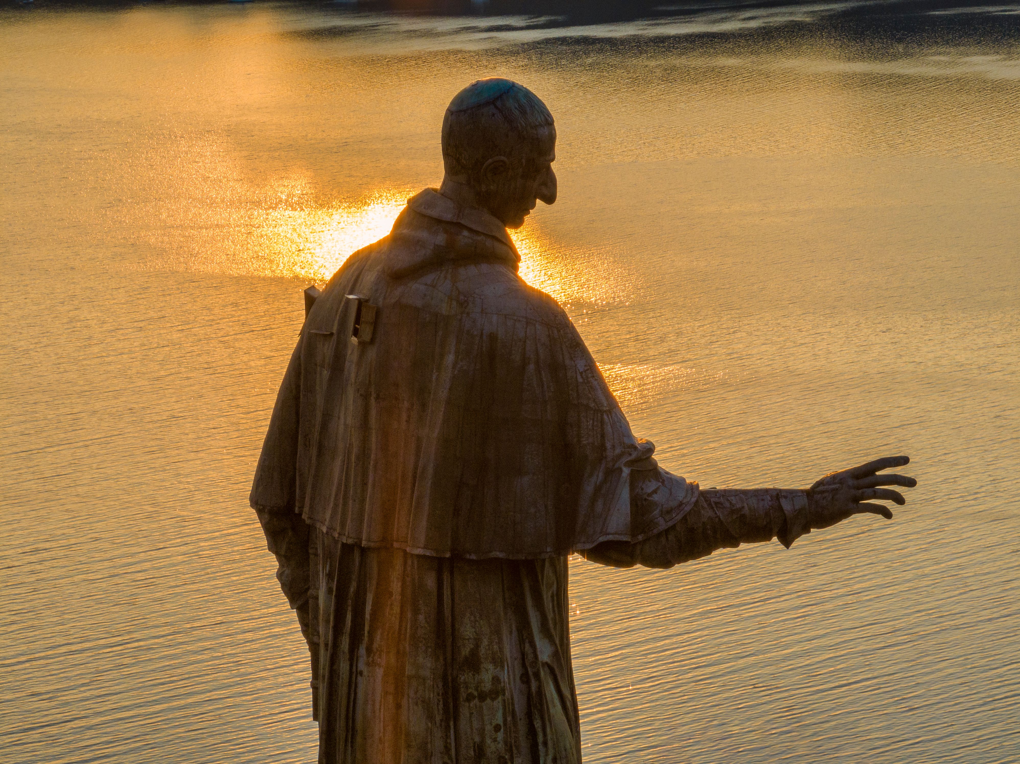 A bronze statue gracefully extends over a shimmering lake during golden sunset.