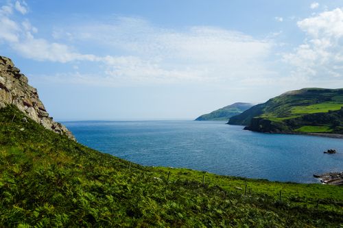 Free Beautiful coastal landscape showcasing lush green hills and a serene blue ocean under a sunny sky. Stock Photo