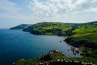 Breathtaking view of a lush green coastal landscape with rocky bays under a bright sky.