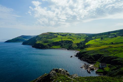 Free Stunning coastal landscape with lush green hills and blue ocean under a cloudy sky. Stock Photo
