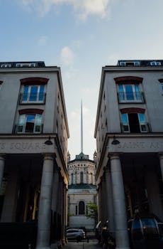 Symmetrical view of modern buildings framing a distant spire under a clear sky.