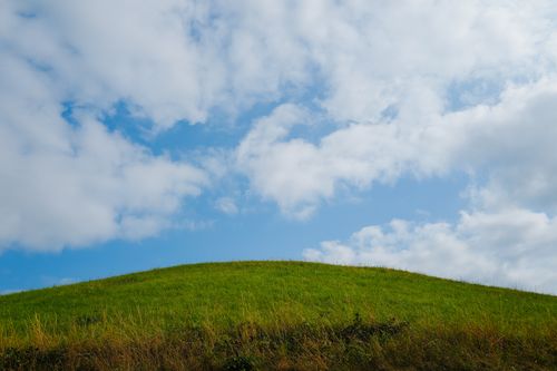 Free A vibrant green hill set against a bright blue sky with fluffy clouds, showcasing natural beauty. Stock Photo