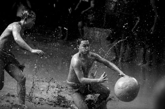 Energetic scene of two men playing soccer in the mud, captured in black and white