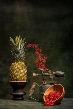 Vintage still life featuring a pineapple, red berries, and rustic objects against a dark backdrop.