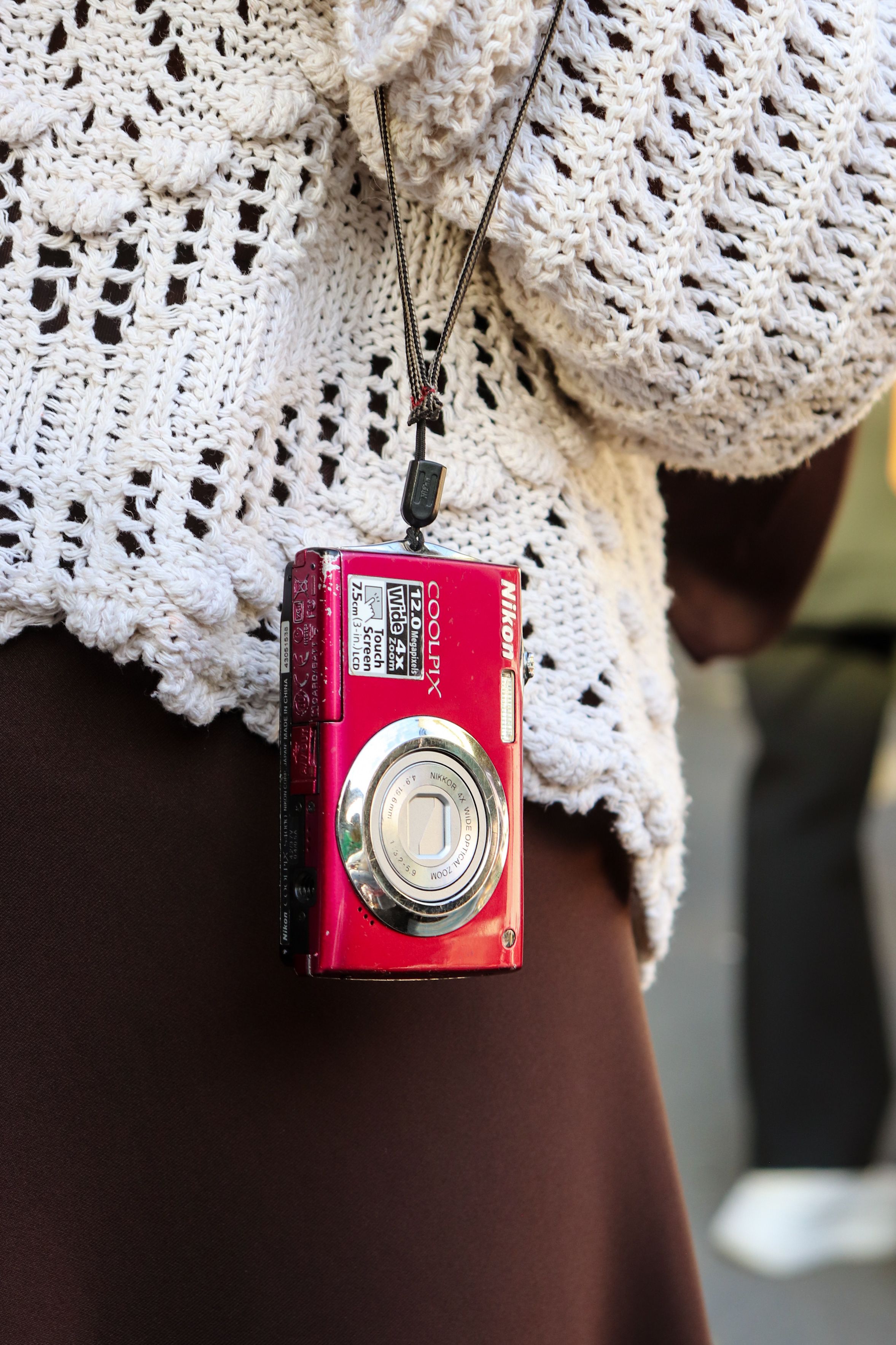 Close-up of a red compact camera hanging from a crochet sweater.