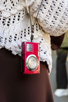Close-up of a red compact camera hanging from a crochet sweater.