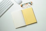 工作区干净整洁，从上往下看，配有键盘、鼠标、时尚眼镜和一台打开的笔记本