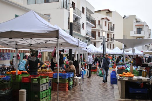 Busy outdoor market with vendors and shoppers in a city plaza under tents.