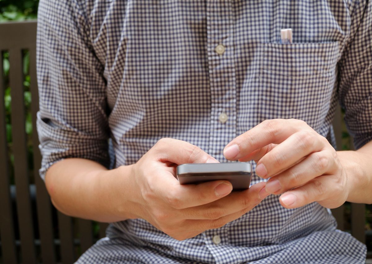 Akıllı telefonu elinde tutan ve ekrana bakan genç erkek