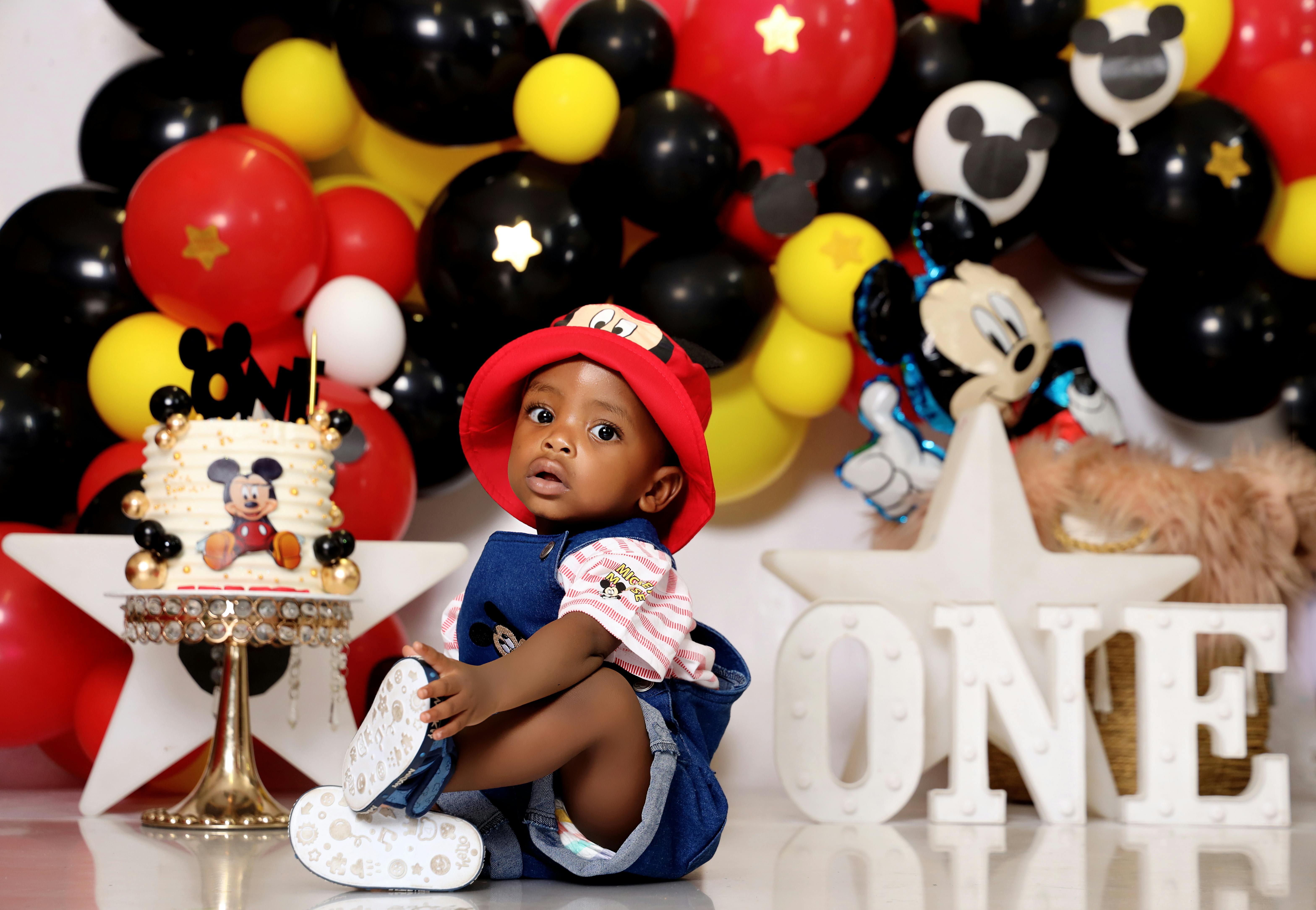Charming baby in Mickey Mouse theme at first birthday party with colorful decor.