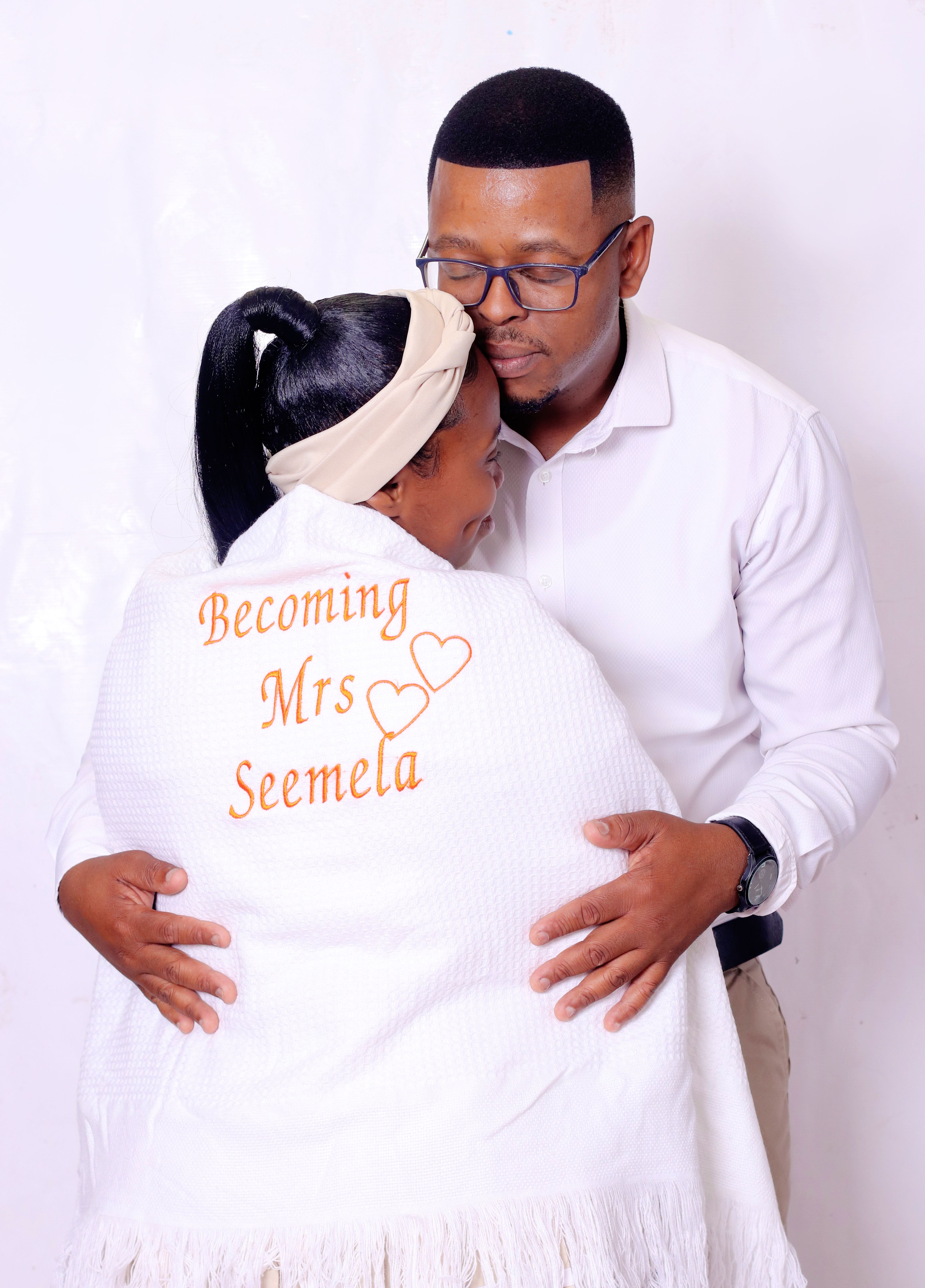 Couple embracing with personalized shawl reading 'Becoming Mrs Seemela', celebrating engagement.