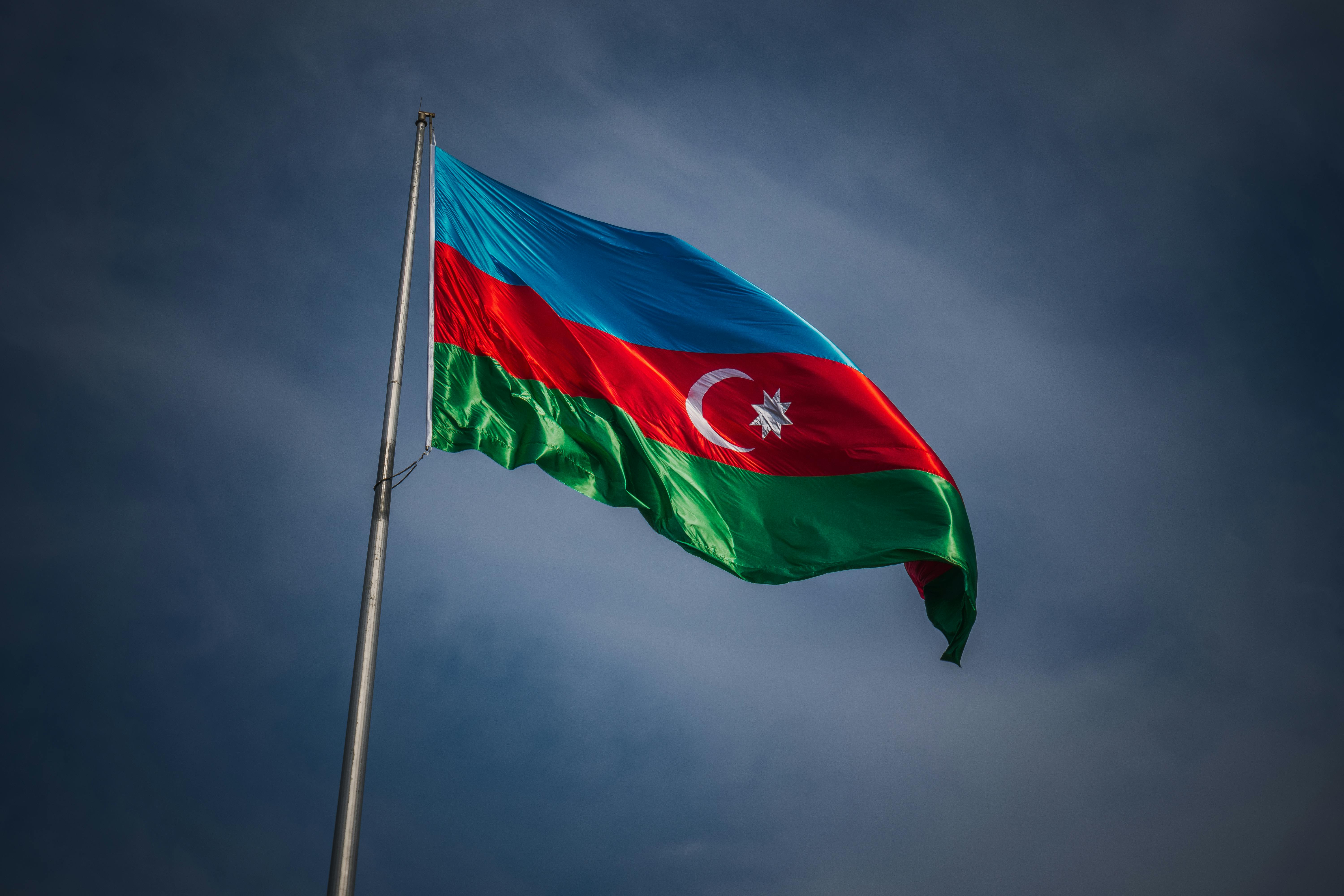 A vibrant Azerbaijani flag flutters proudly on a flagpole against a clear blue sky, symbolizing national pride.