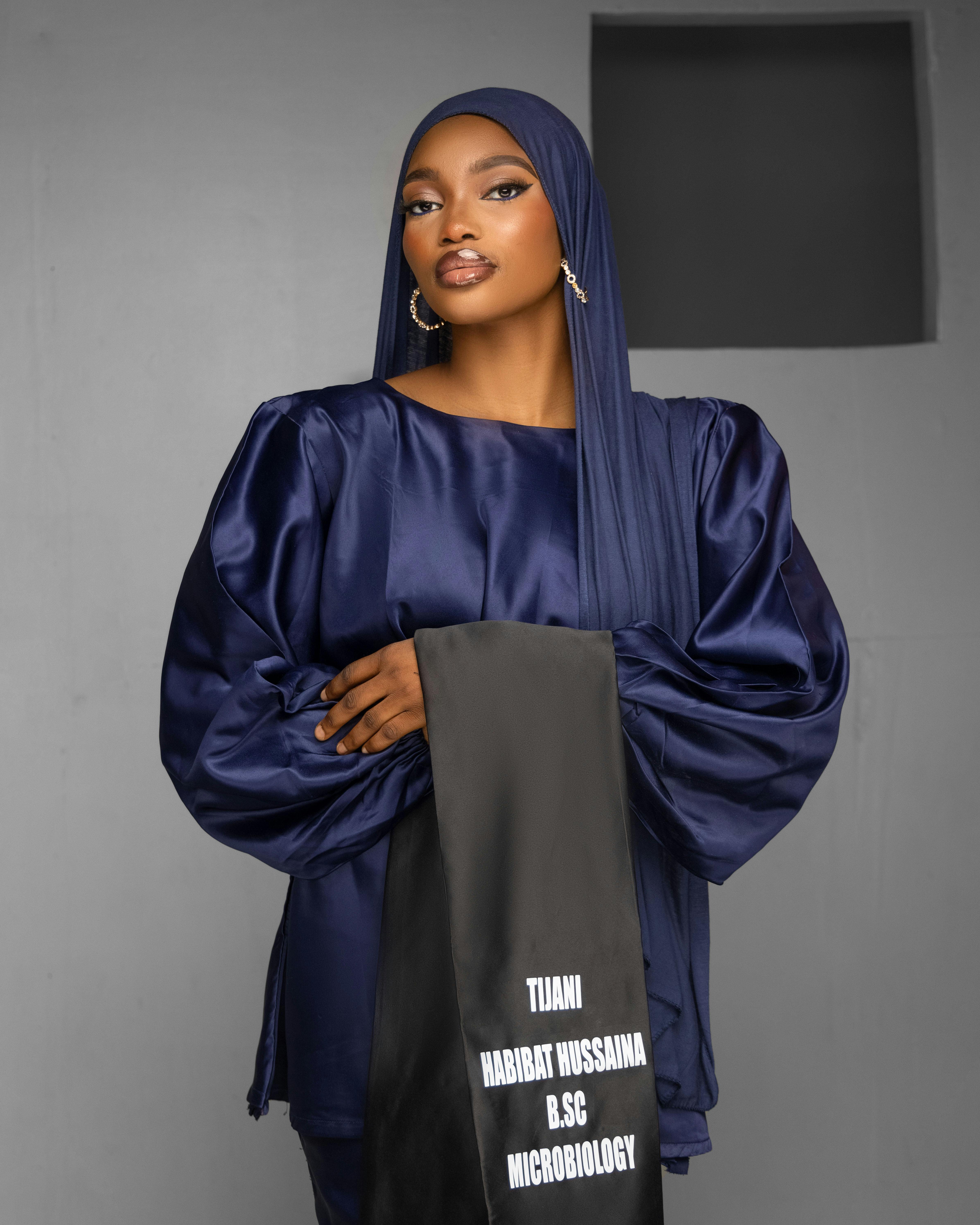 Striking portrait of a woman in navy silk attire holding a customized graduation stole.