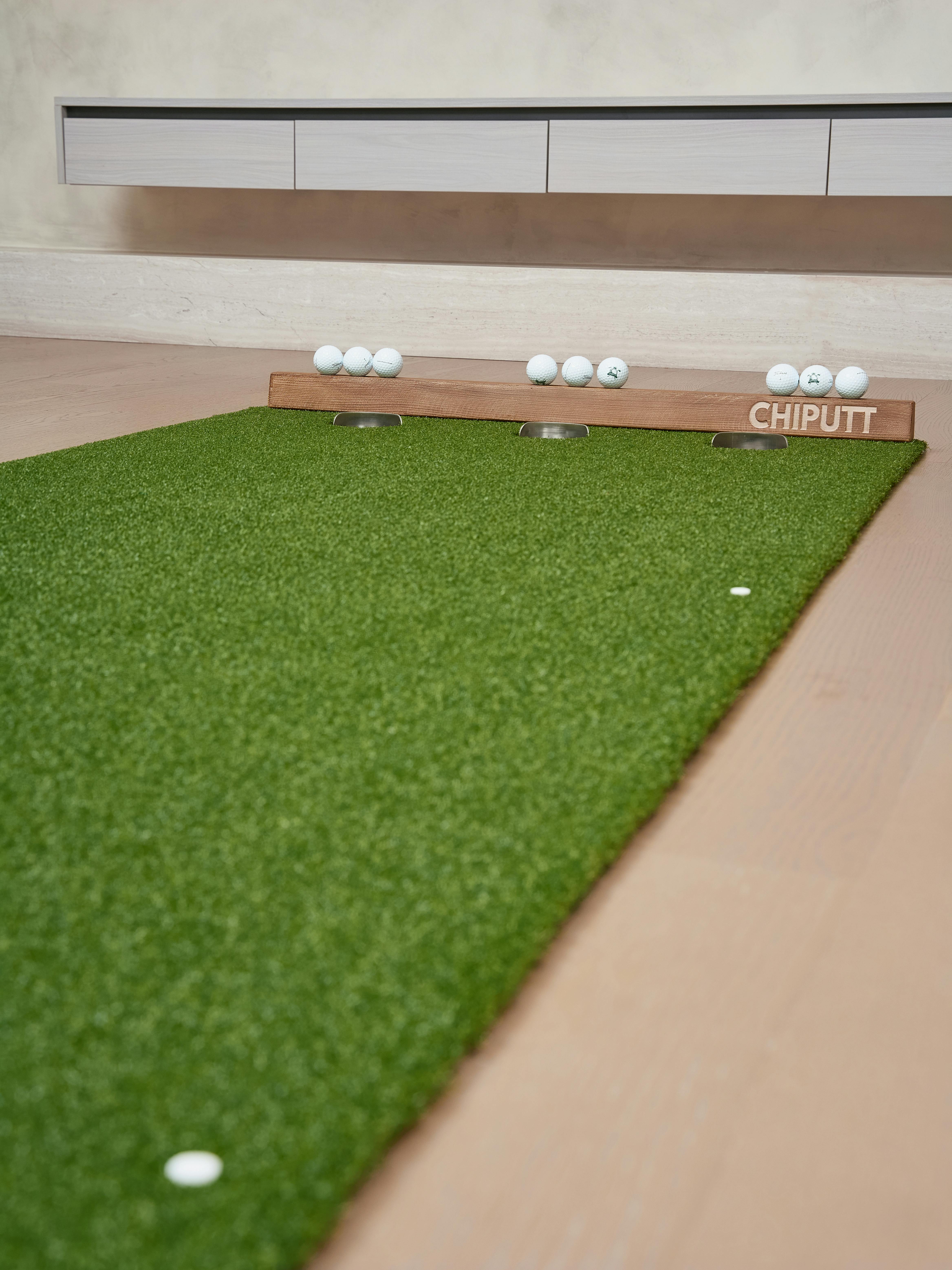Indoor golf practice setup with artificial turf putting mat and golf balls for training.