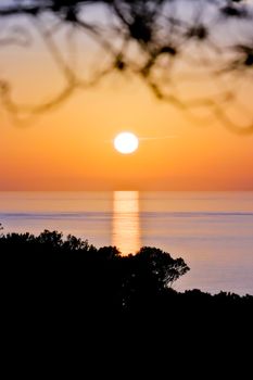A tranquil sunset view with silhouette of distant trees against a calm ocean horizon.