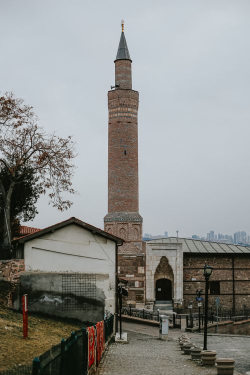 Free Tall brick minaret amidst city buildings under cloudy skies, showcasing cultural architecture. Stock Photo