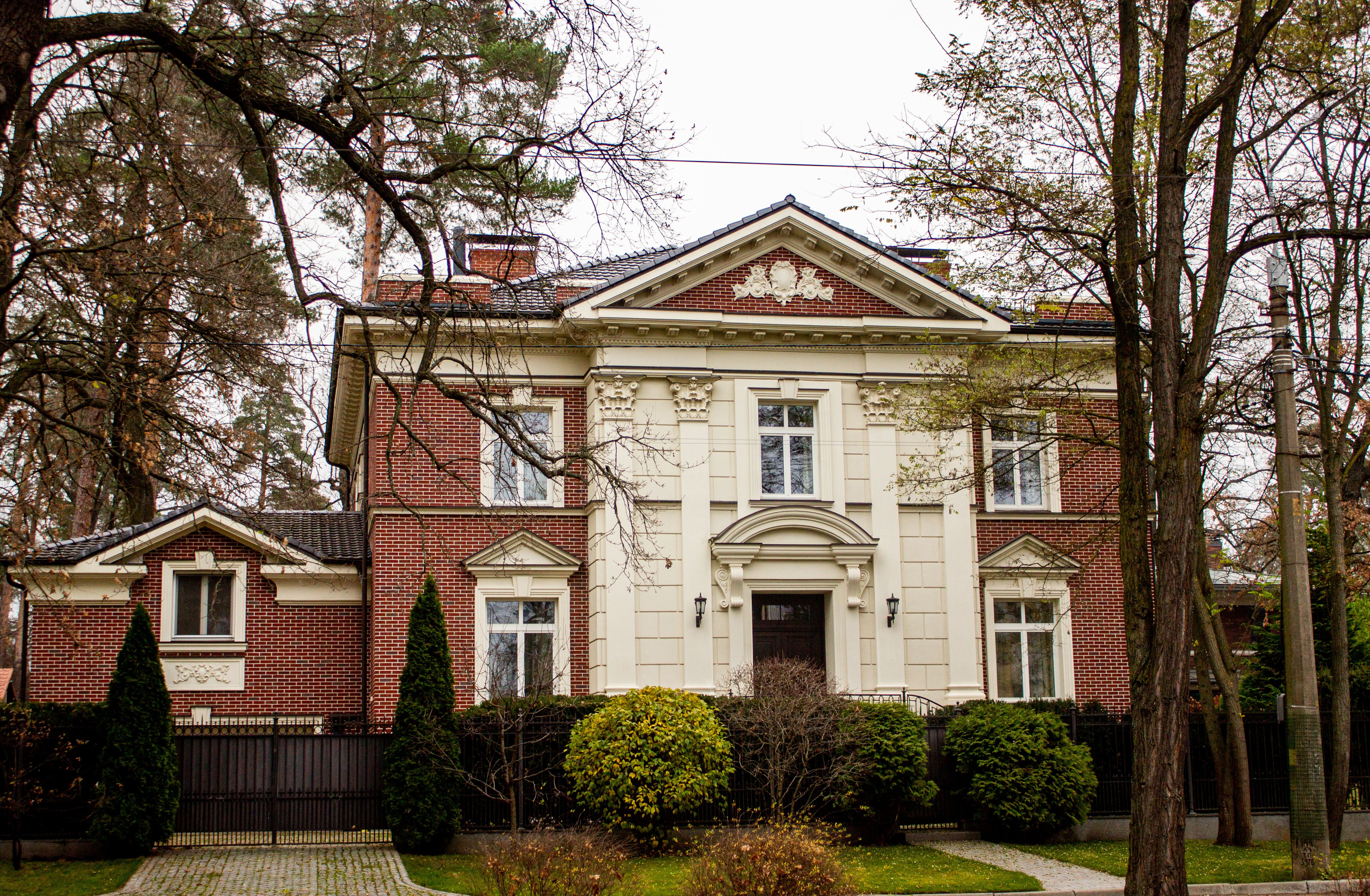 A classic brick house with ornate detailing surrounded by autumn trees and nature.