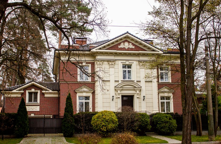 A classic brick house with ornate detailing surrounded by autumn trees and nature.