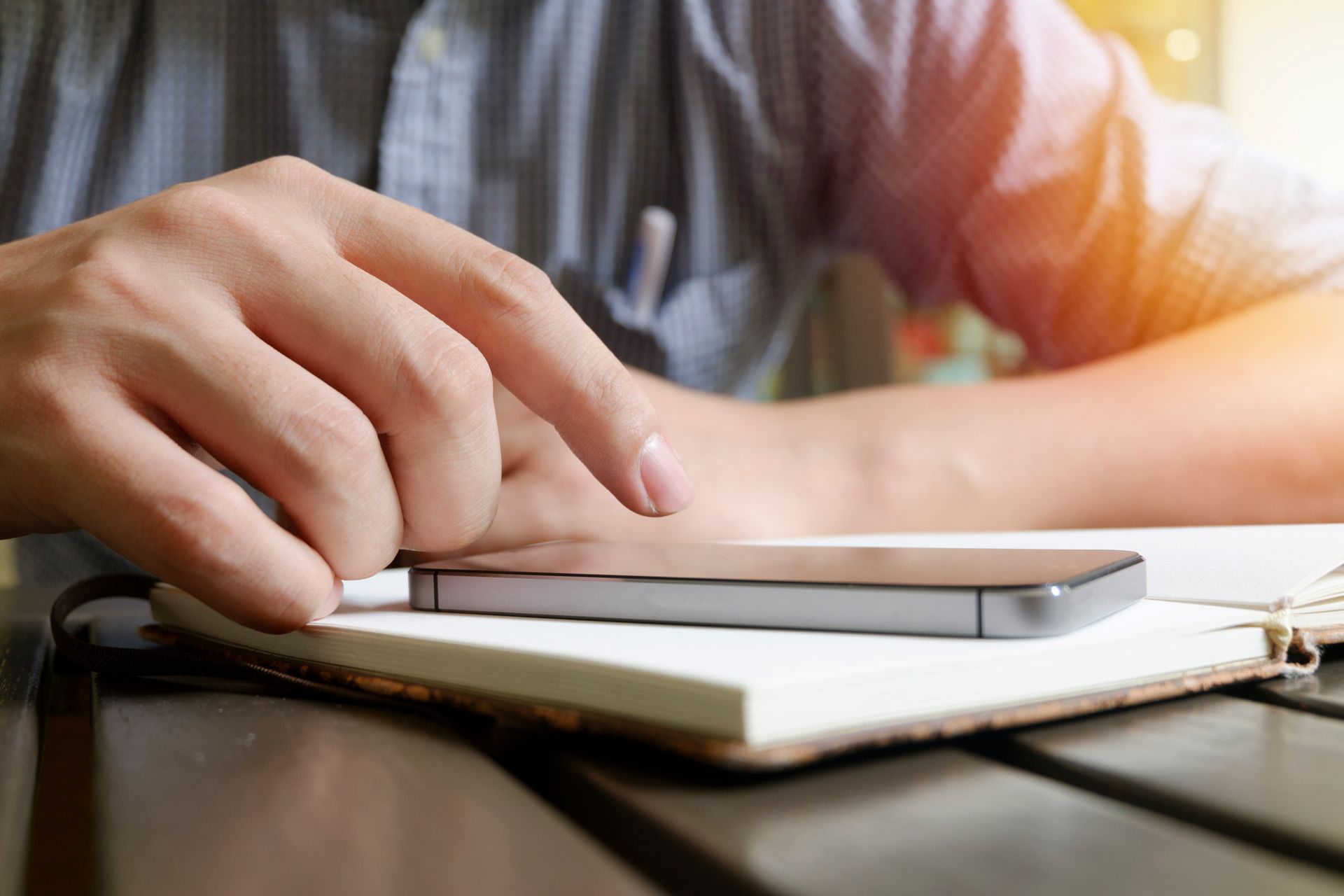 A close-up view of a hand interacting with a smartphone and notebook on a desk.