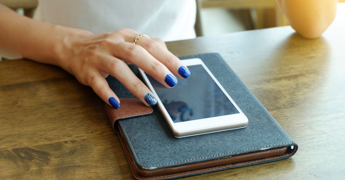 Mão de mulher com unhas azuis no smartphone e caderno, retratando tecnologia moderna e estilo.