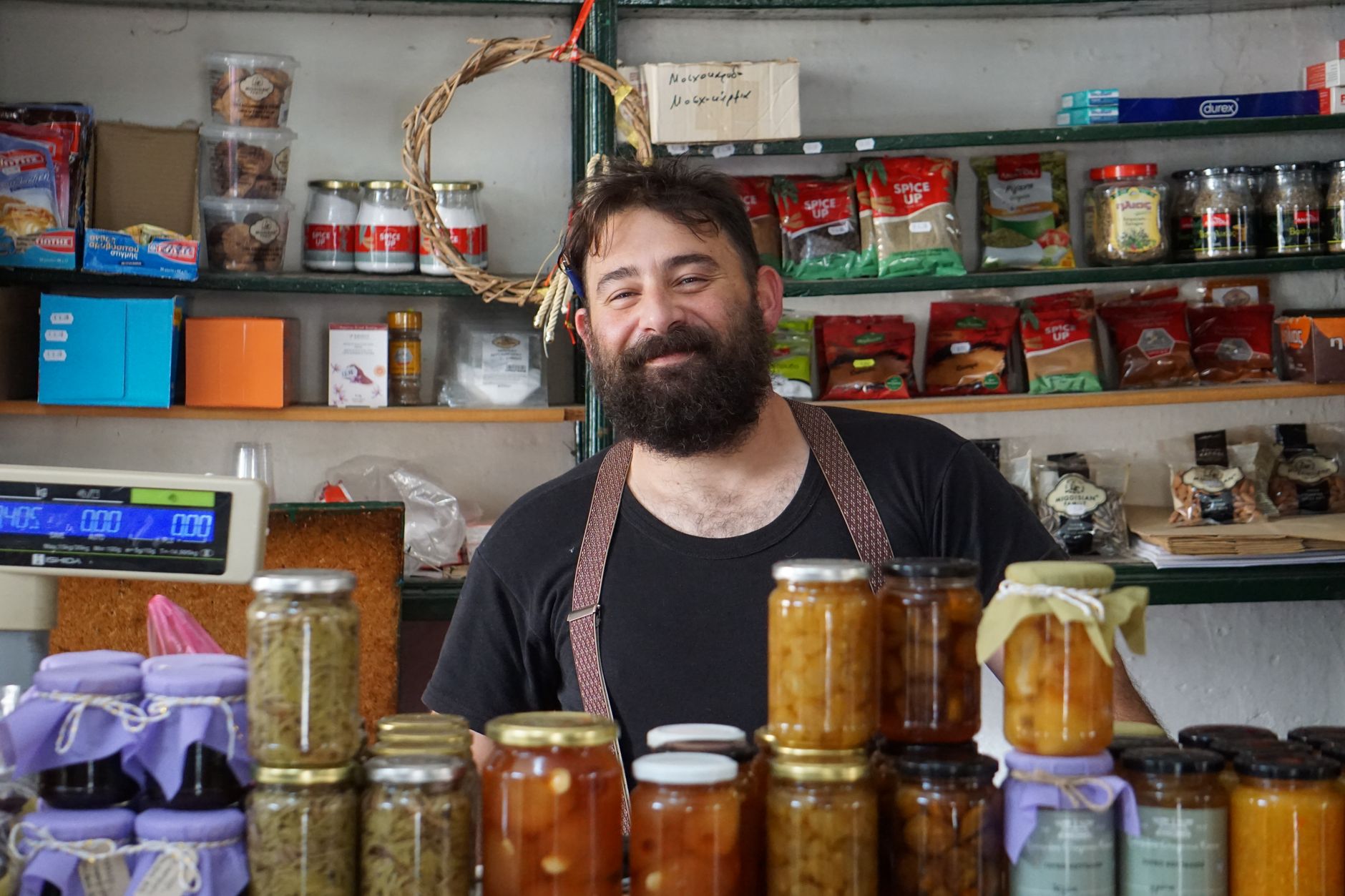 A friendly shopkeeper standing behind shelves of homemade preserves in a small shop