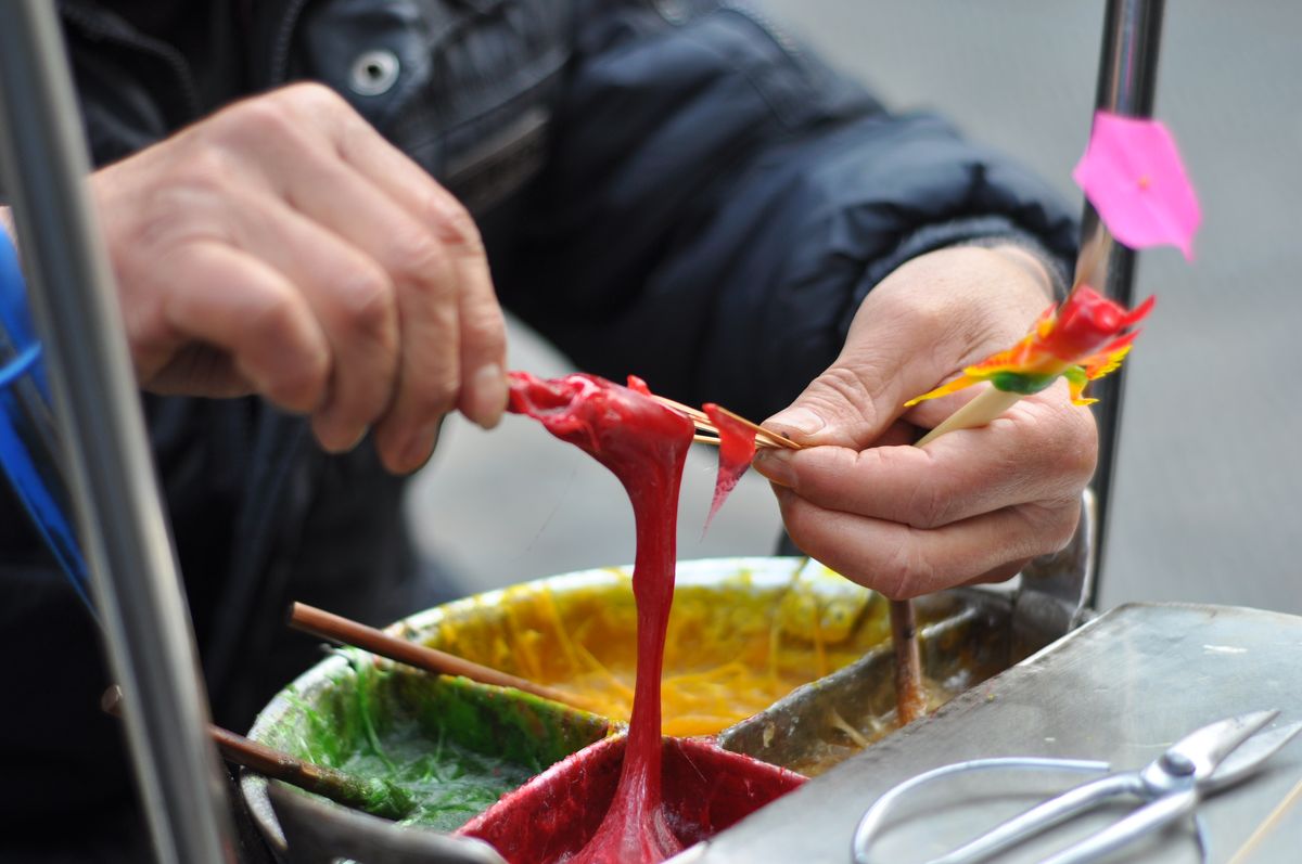 Street artist crafting colorful sugar figurines live in an urban setting, showcasing traditional techniques.