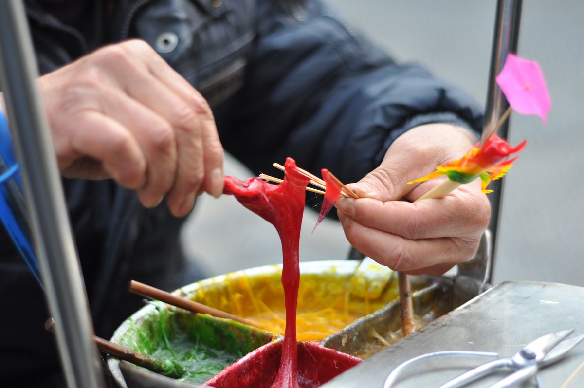 Close-up of hands crafting colorful traditional sugar art in an outdoor setting.