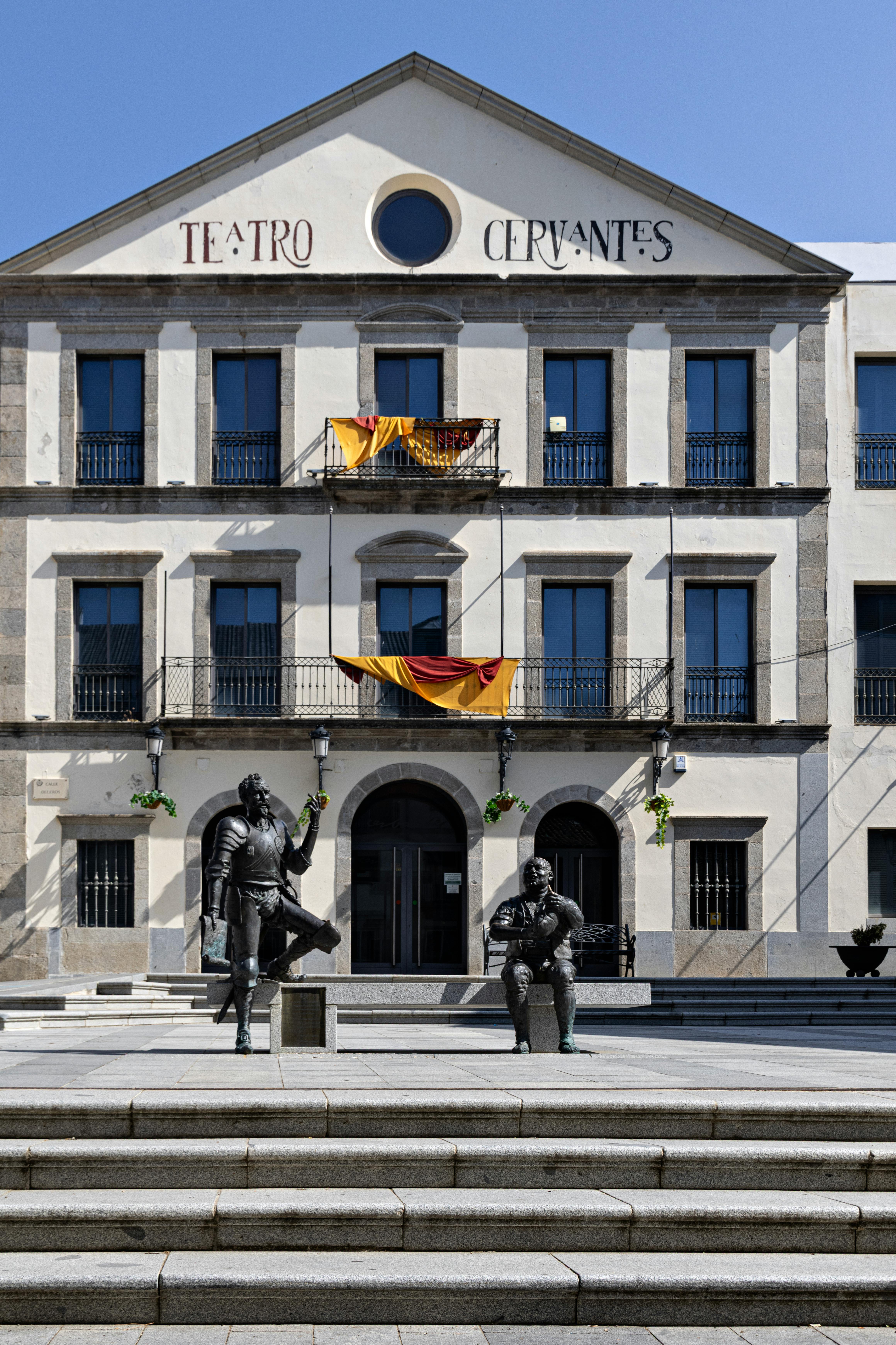 The façade of Teatro Cervantes in Alcalá de Henares with Don Quixote statues on a clear day.