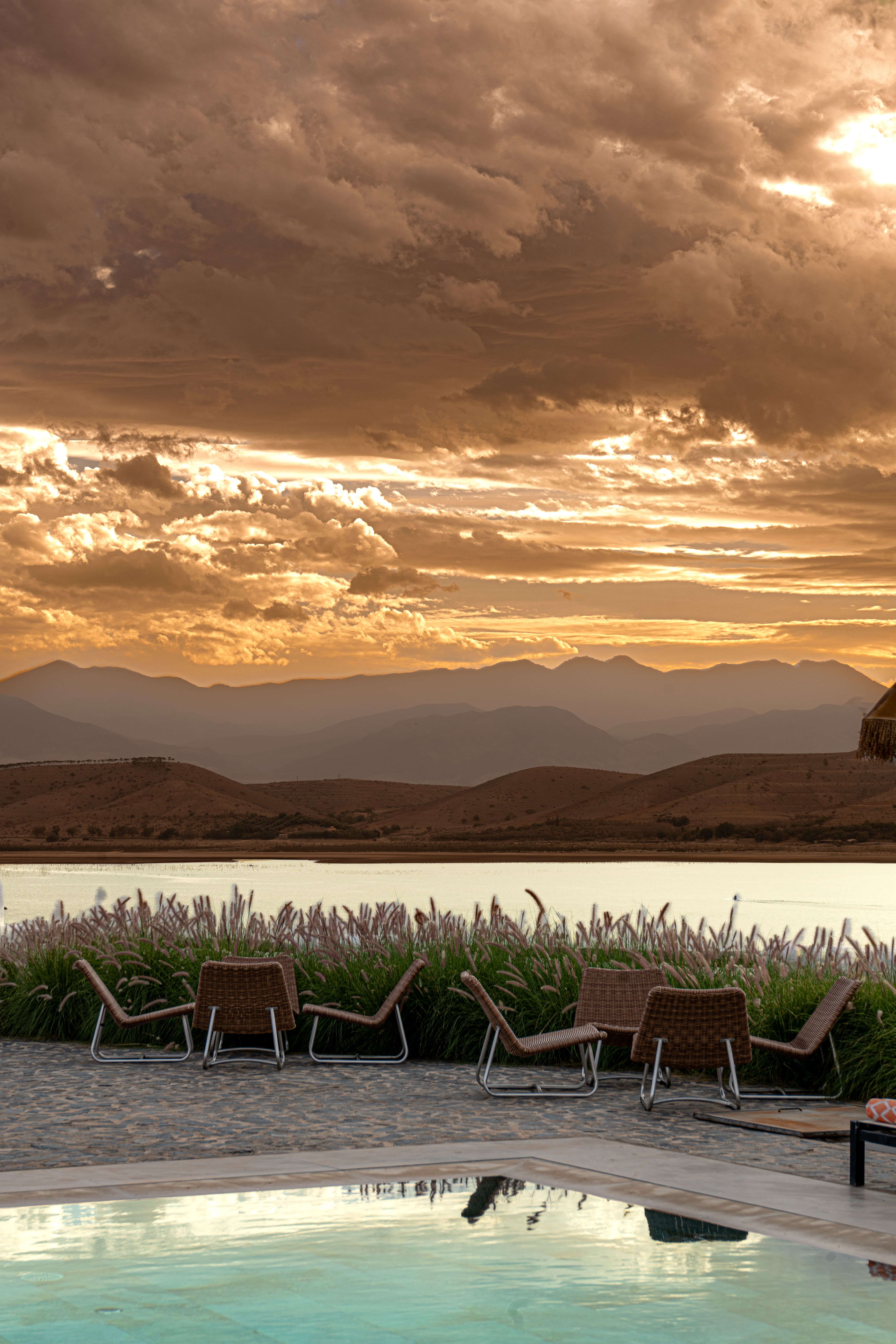 Stunning sunset by a mountain lake with lounge chairs and tranquil water reflections.