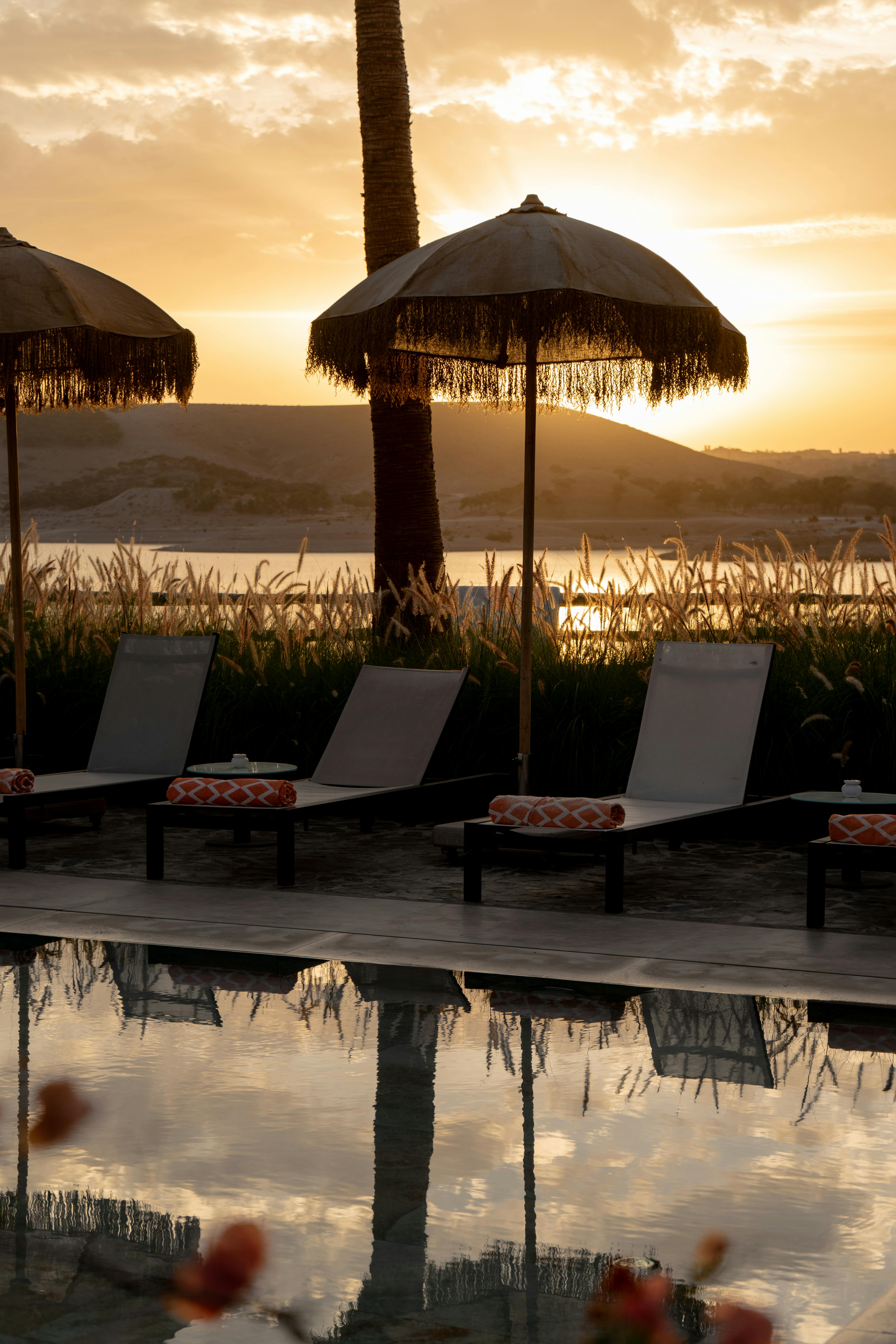 Serene sunset view from a tropical resort, featuring poolside lounge chairs and fringed umbrellas.