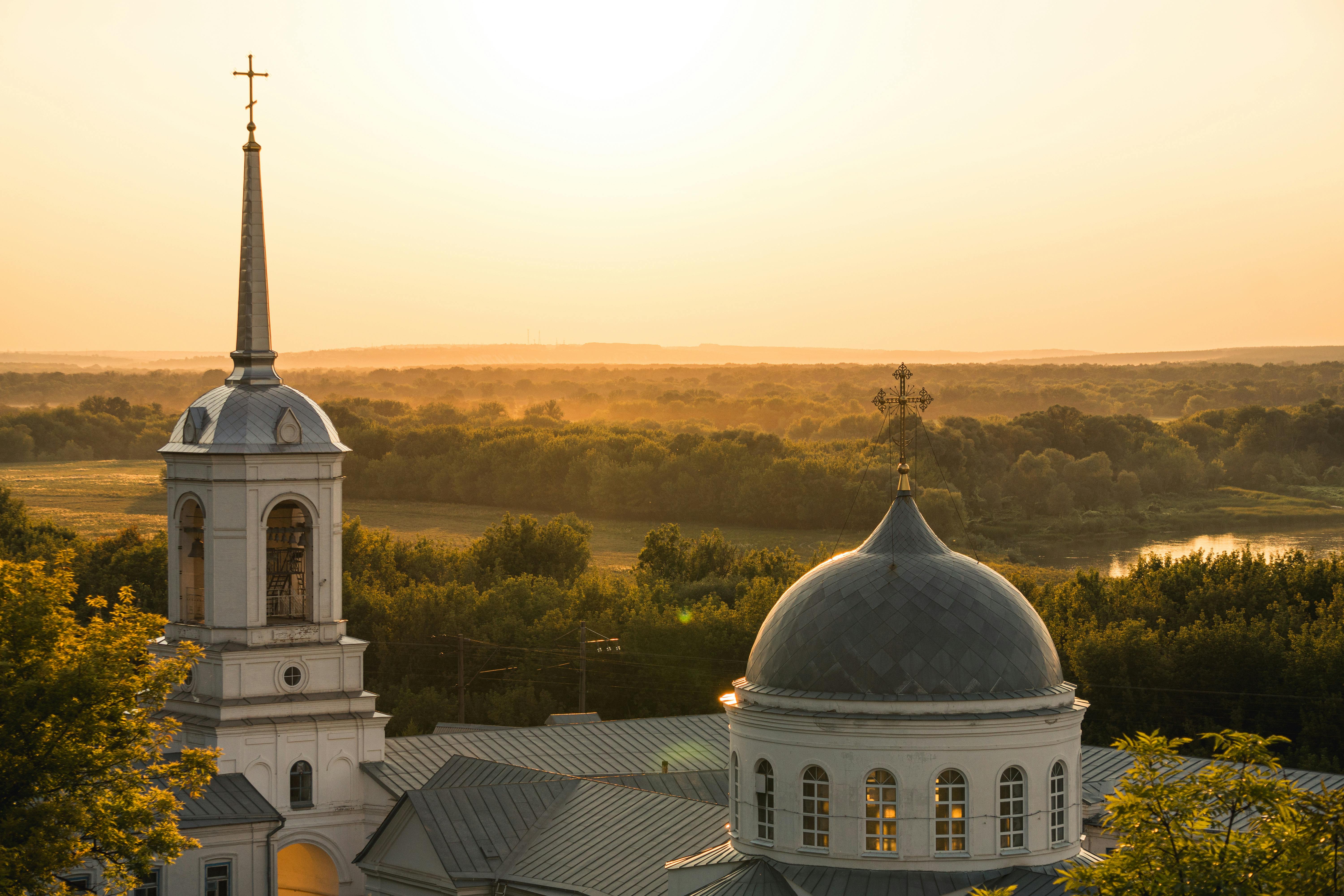 Serene sunset view over a historic church dome amidst lush greenery.