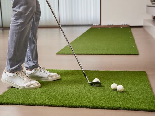 Free A golfer practices putting indoors on artificial turf with golf balls and club. Stock Photo