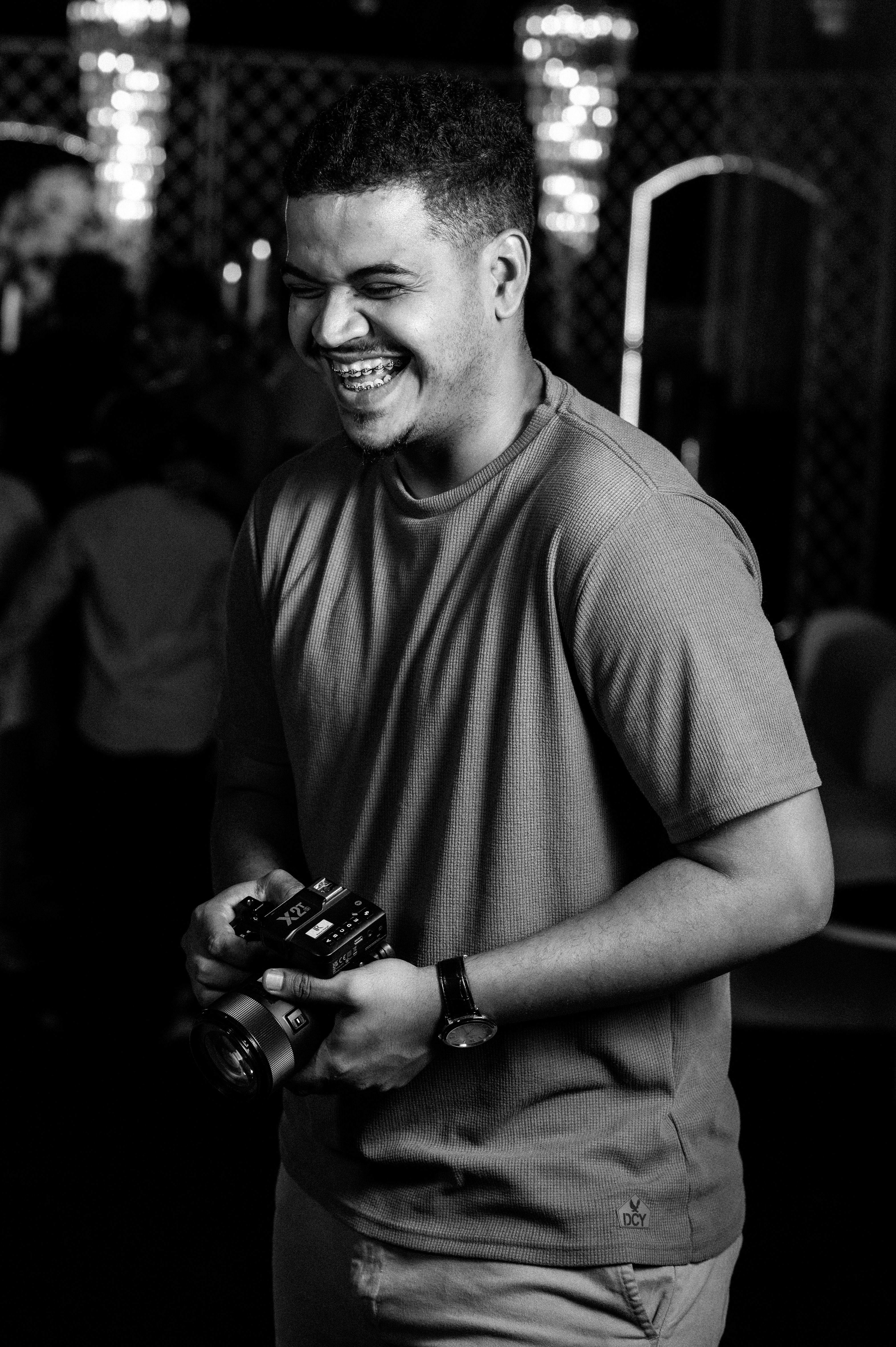 Black and white photo capturing a young photographer joyfully holding a camera with a bright smile.