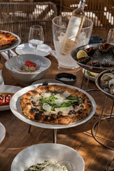A table set with gourmet pizza, seafood, and chilled wine, capturing a sunny Italian dining experience.