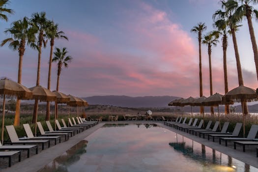 Tranquil poolside scene at sunset with palm trees and lounge chairs, perfect for relaxation.
