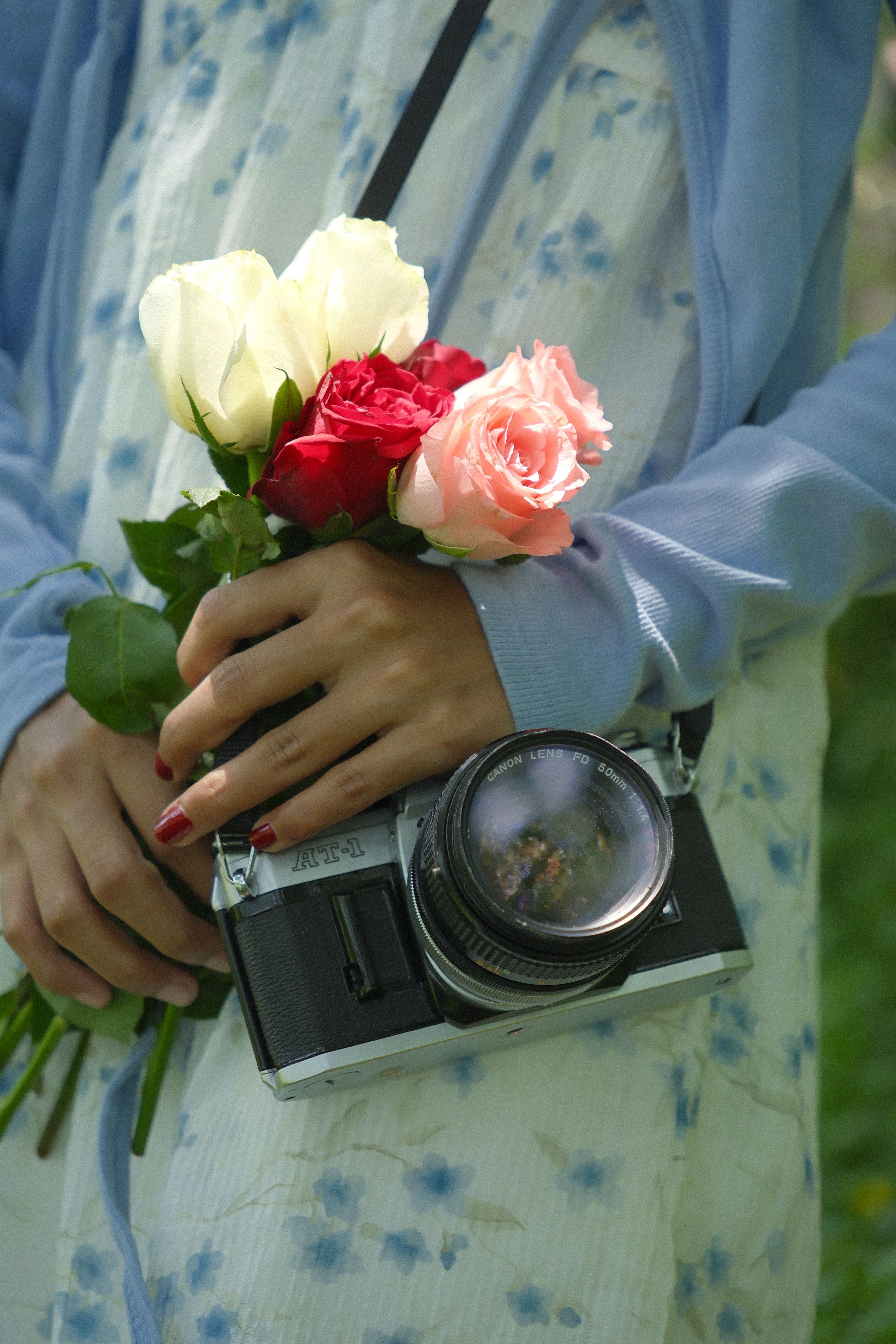 A close-up of a person holding roses and a vintage camera, showcasing a blend of technology and nature.