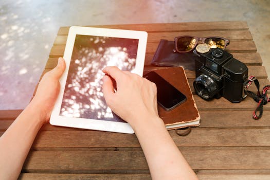 平板电脑放在户外的木桌上，旁边有相机、手机和太阳镜