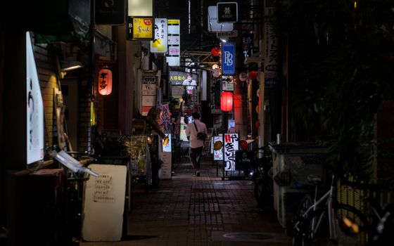 A person walking through a dimly-lit alley in Kobe, Japan, with lanterns and vibrant signs at night.