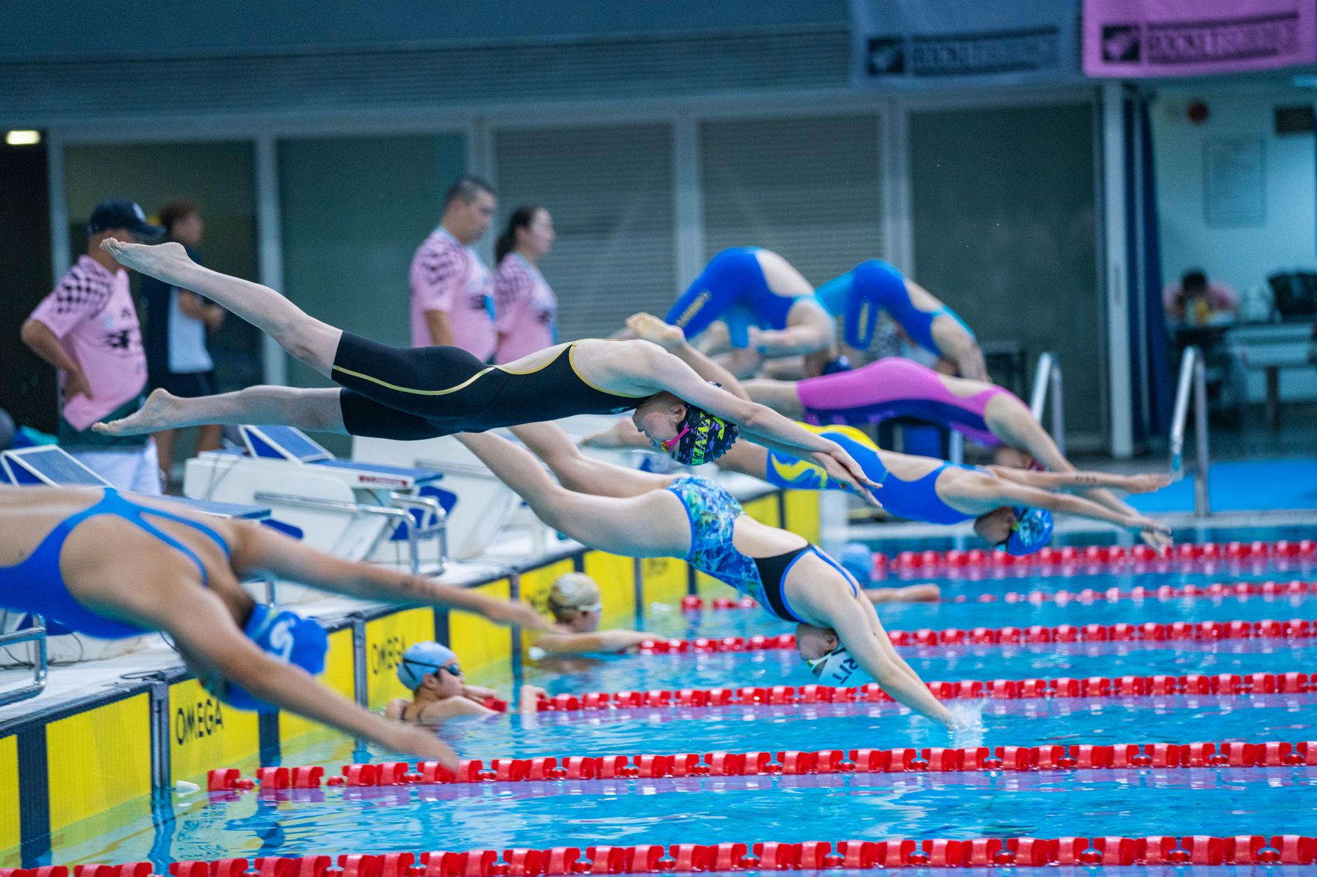 Athletes diving into a swimming pool at the start of a competitive race indoors.