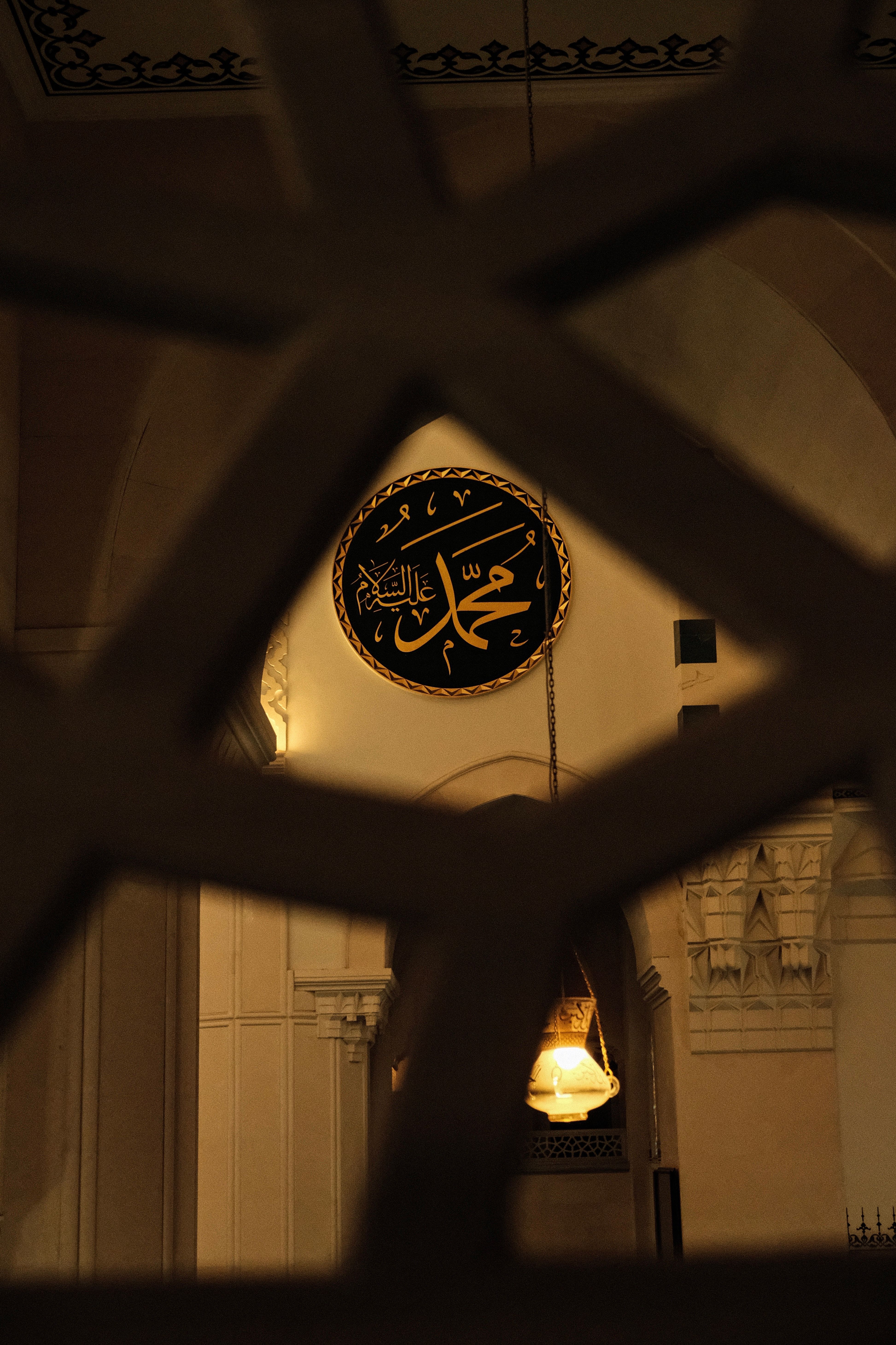 Elegant Islamic calligraphy inside a mosque, viewed through latticework, capturing spiritual essence.