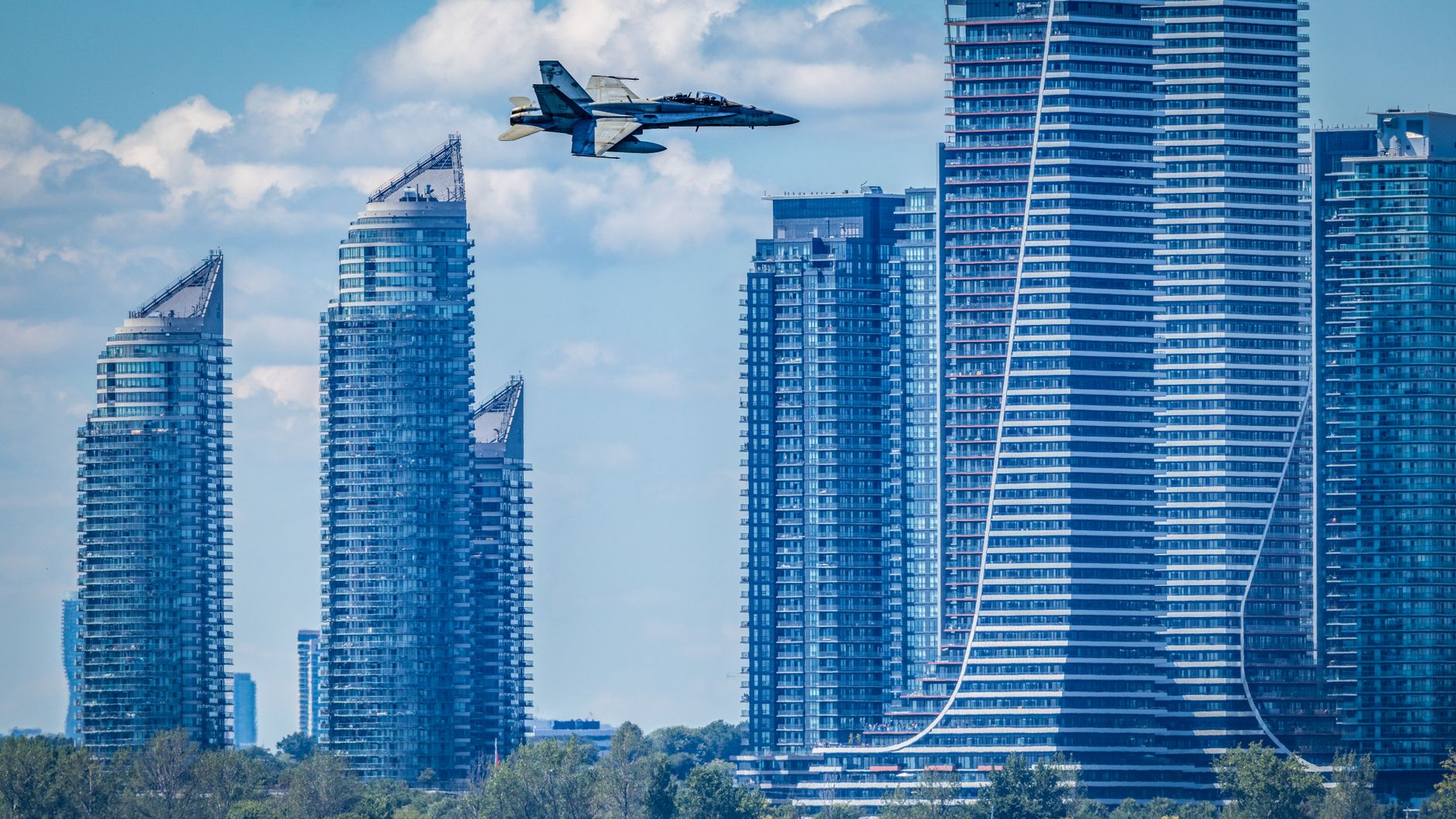 A jet plane soaring past futuristic skyscrapers under a blue sky.